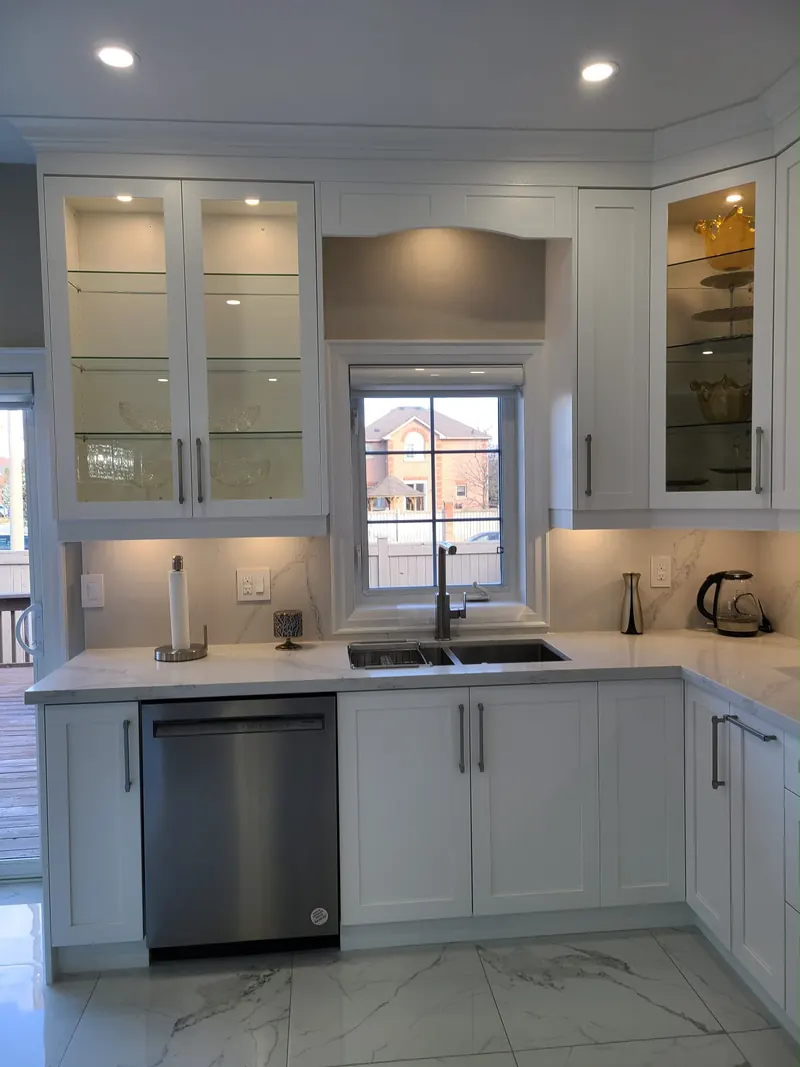 Completed kitchen renovation with white cabinets, lit glass-door uppers and a veined backsplash