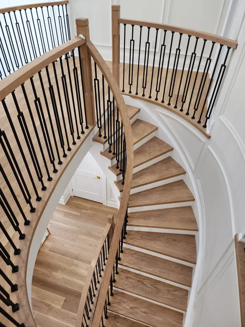 Curved staircase with wood treads, white risers and black metal balusters, seen from above